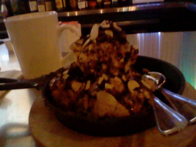 A cast iron pan with 5 balls of mocha ice cream. It is drizzled in caramel with almonds on top. Beside it is a refilled cup of coffee.