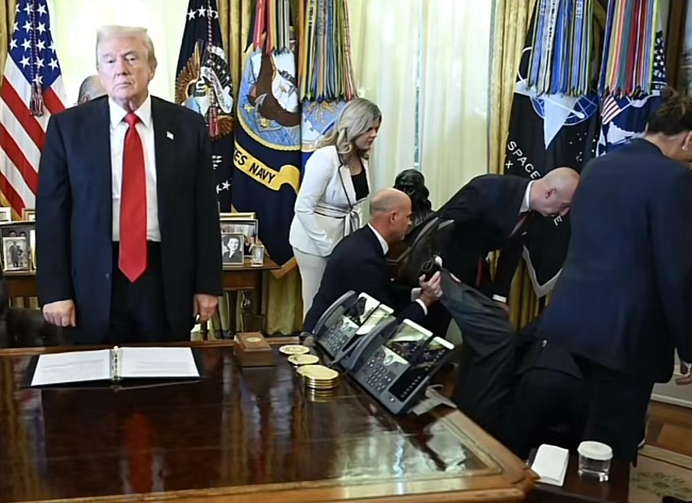 Inside the Oval Office, a man lies on the floor being helped by others after appearing to pass out, while Donald Trump stands front and center at the desk with a neutral expression, seemingly unfazed by the situation unfolding behind him, wondering why he’s not the center of attention. 