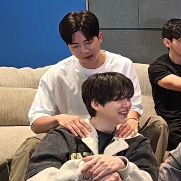 screenshot of the same scene moments later: namjoon is now looking at yoongi and yoongi is smiling a gummy smile. namjoon's hands rest closer to yoongi's neck