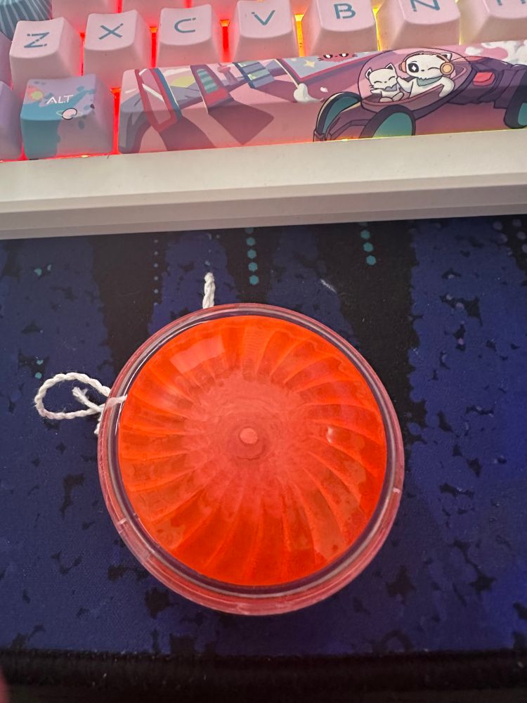 a photo of a red yo-yo sitting on a desk. it resembles a late 90’s-early 2000’s iMac or similar Apple computer.