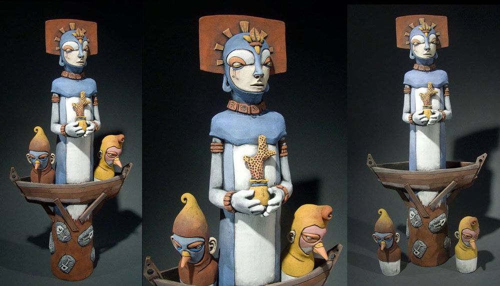 A tall cylindrical figure that tapers toward the top. Half way up the form there is a boat that the cylinder passes through. On the left and right side of the boat there are small figures looking down over the sides of the boat. the small figures have no arms and legs but are wearing masks that make them look bird like. The central figure is topped with a head that has closed eyes and looks peaceful. She is wearing a flat headdress that is rectangular with rounded corners. The central figure has arms that bend toward the chest. Where the hands meet she is holding a small bag with a brightly colored piece of corral. As you follow the center cylinder down below the boat there are small carvings of what look like fish skeletons embedded in the cylinder's wall. 