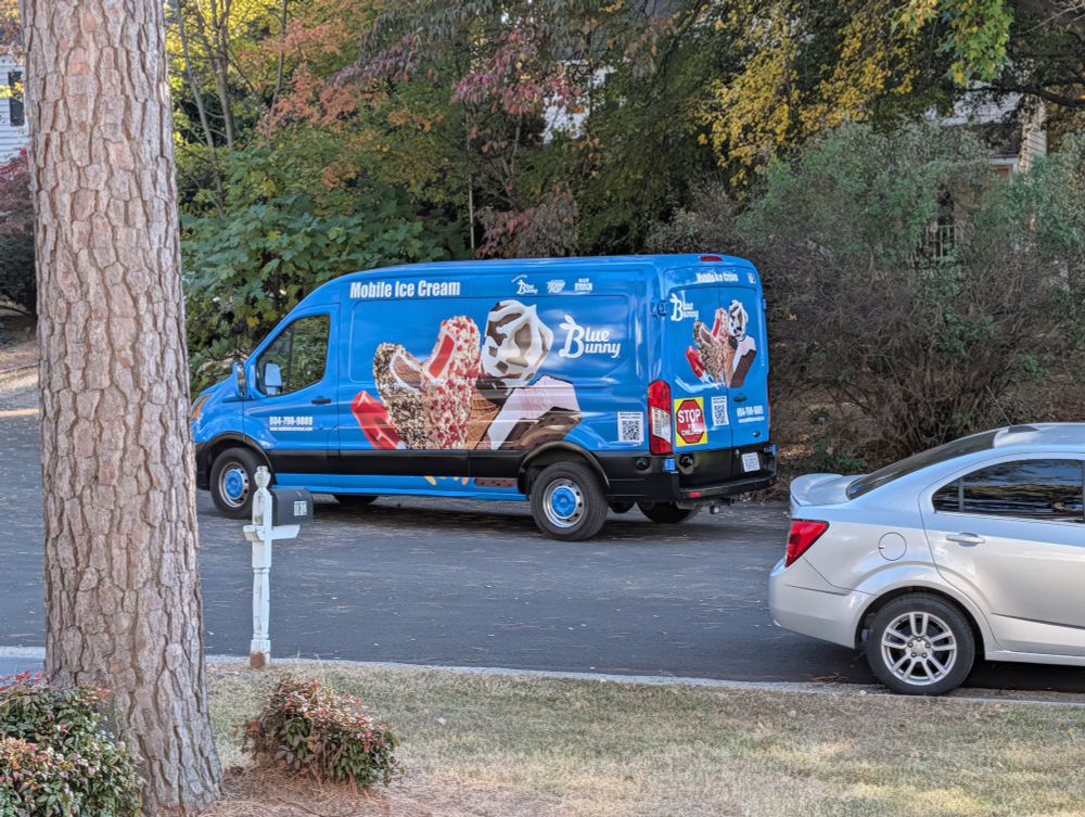 A blue ice cream van traveling down a neighborhood street.
