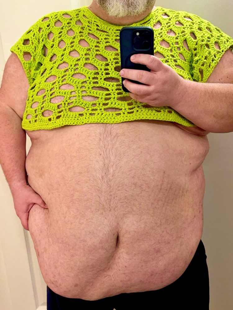 A photo of me in a neon green crocheted crop top holding my belly