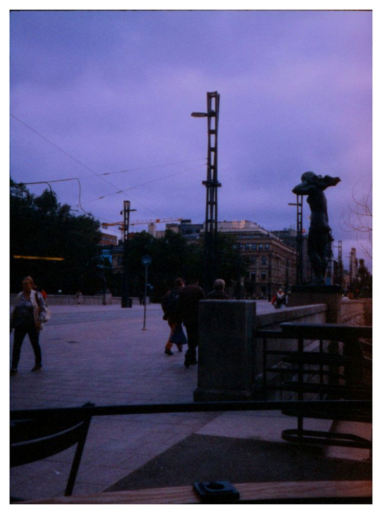 The people, statues and electric poles on the Häme bridge, as seen from within the Fazer Café.