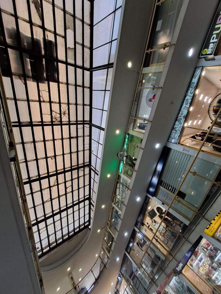 Photo inside of a Chilean mall. A huge lightbox spans its ceiling, and some stores can be seen to the right.