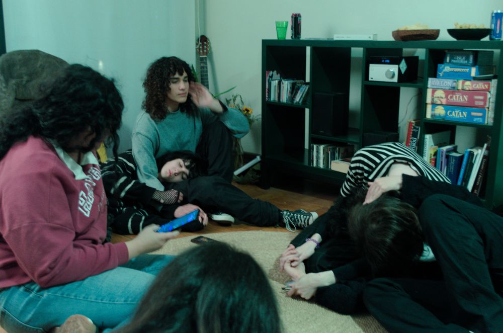 A photo of a living room. I am to the right of the picture, making out with my girlfriend while holding hands. To the left, a girl is looking at her phone, and one has her head laying on the lap of another one.