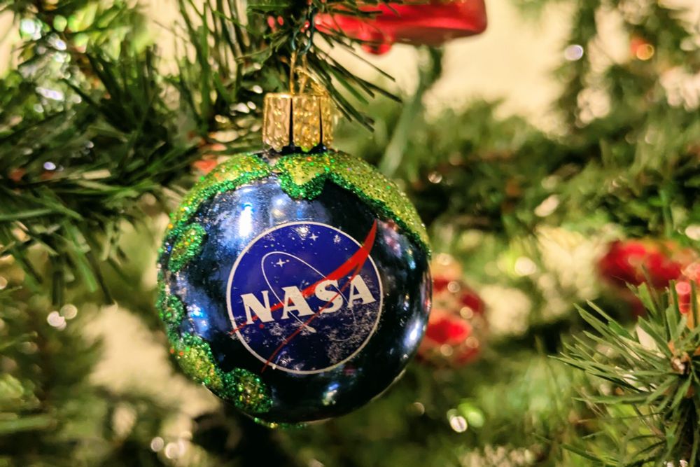 NASA globe ornament with logo on deep shiny blue background with glitter green continents on an artificial evergreen Christmas tree