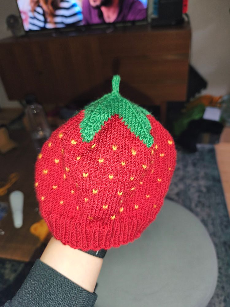 Eine selbstgestrickte Kindermütze die aussieht wie eine Erdbeere