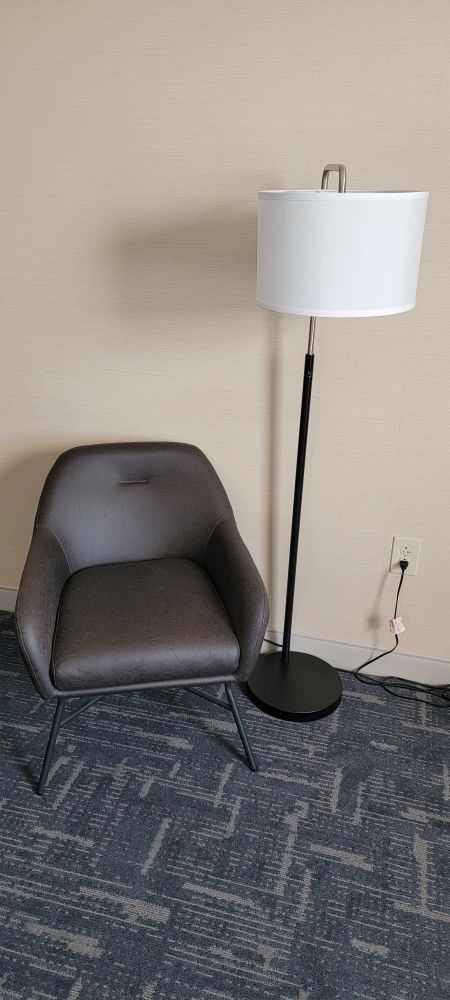 A lonely chair next to a lamp, tucked away into a corner facing the bed