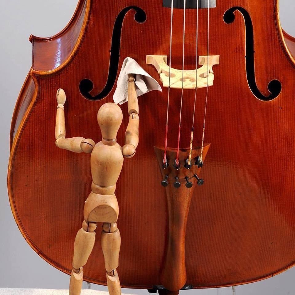 Un pantin de bois essuie un violon avec un chiffon.