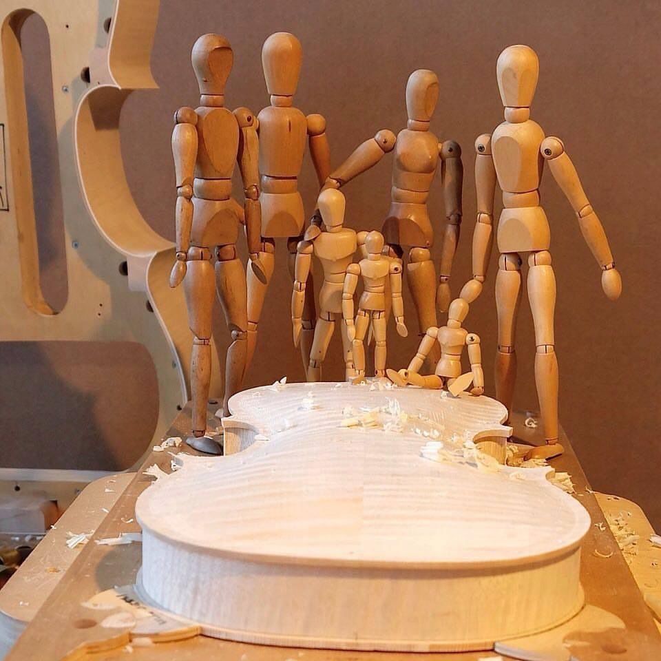 Photo de famille de pantins de bois de différentes tailles sur un violon non vernis avec copeaux.