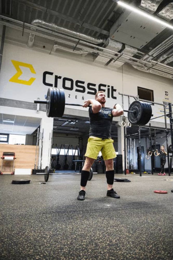 a man is lifting a barbell in front of a wall that says crossfit