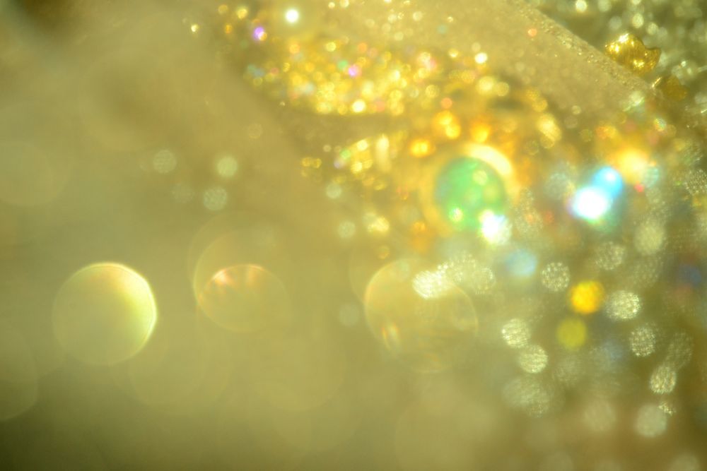 Gold bokeh sparkles in bright clusters of gold, orange, pink, and an occasional hint of blue and green. Some of the bokeh have a patterned effect that is not unlike a fishnet because this is a close-up of glitter tulle and costume jewellery, and the weave of the tulle sometimes gets captured in the bokeh. The effect is bright and hopeful, as though someone magical might be swimming into your life. 