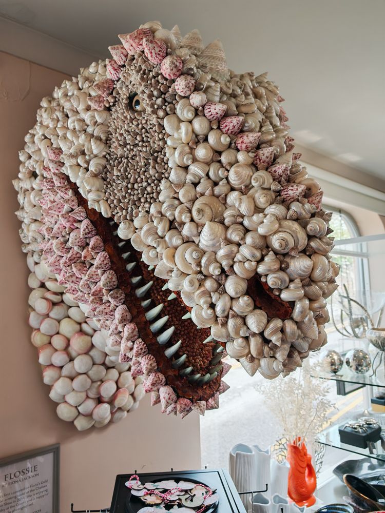 Carnivorous dinosaur head decorated with white and pink shells; right side view.