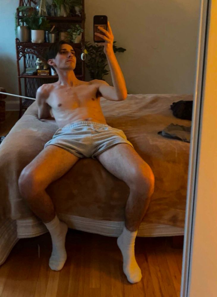 mirror selfie on bed in just grey sweatshorts and white socks 