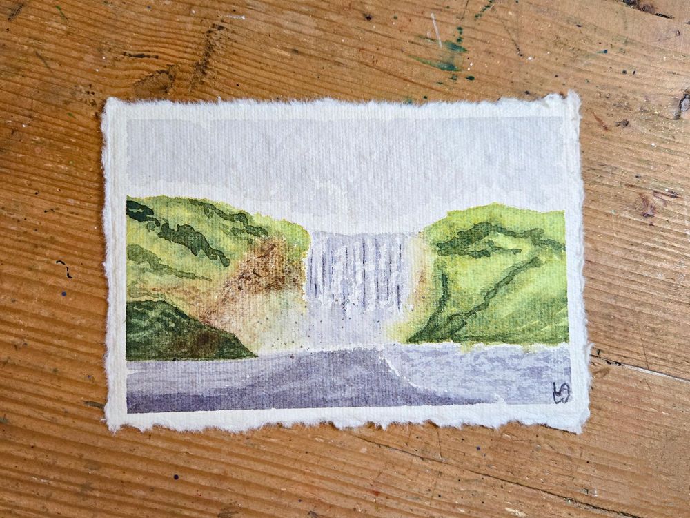 A watercolor painting of a waterfall surrounded by green hills and brown stone. The sky is a light gray, and the foreground is dark gray from the water. 