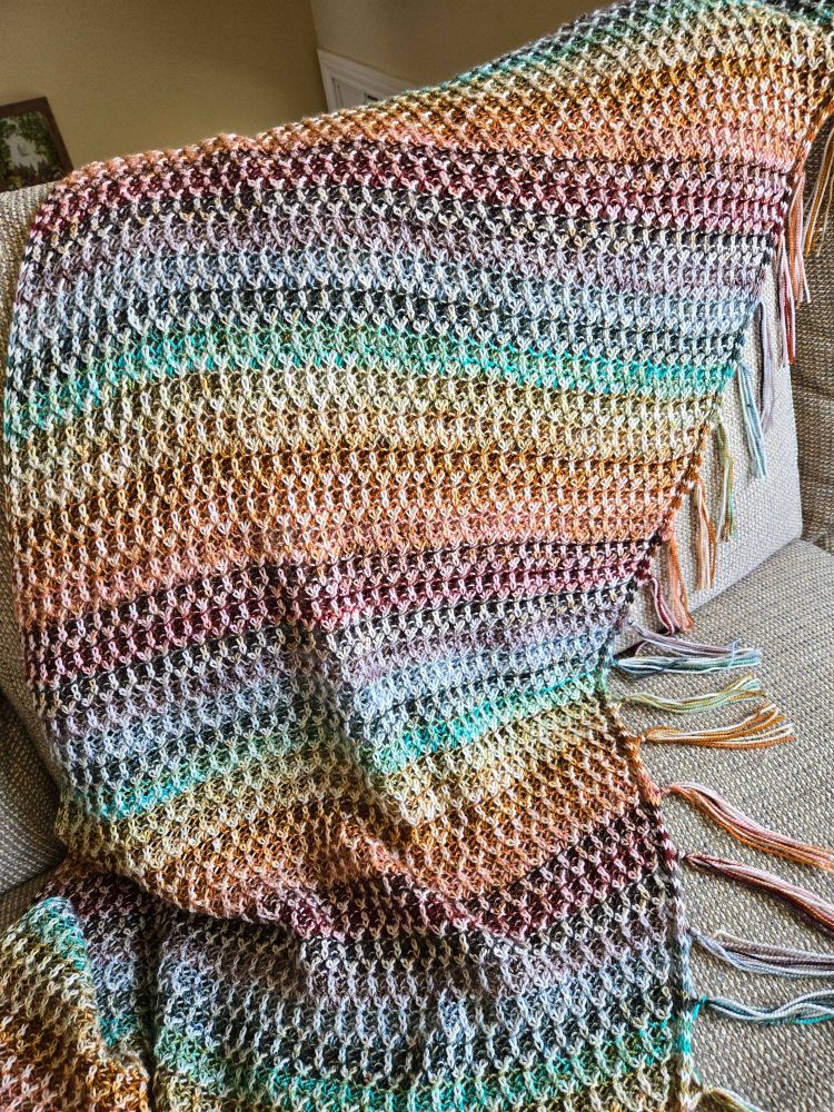 A close-up of the top of the shawl. The shawl is multicolored in a muted rainbow pattern. It is brioche knitted, with the lighter colors forming an elongated honeycomb pattern.