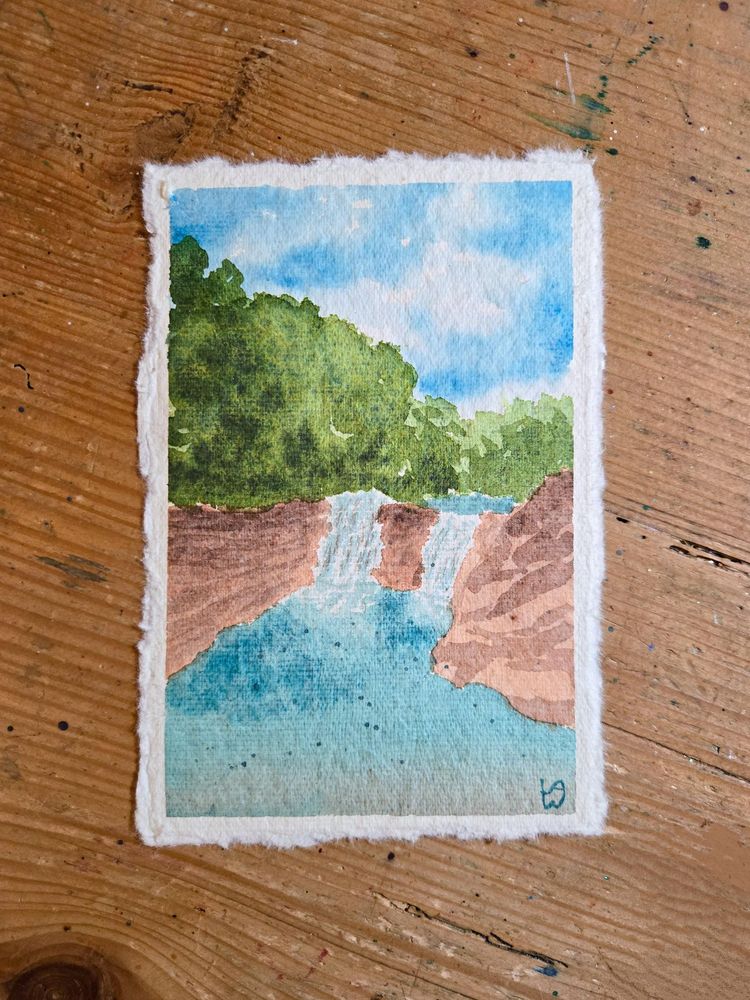 A watercolor painting on textured paper of a couple of small waterfalls surrounded by reddish-brown rocks. The water flows into a turquoise blue pool at the bottom. Above the falls are some loosely painted trees, and above that a bright blue sky with some clouds. 