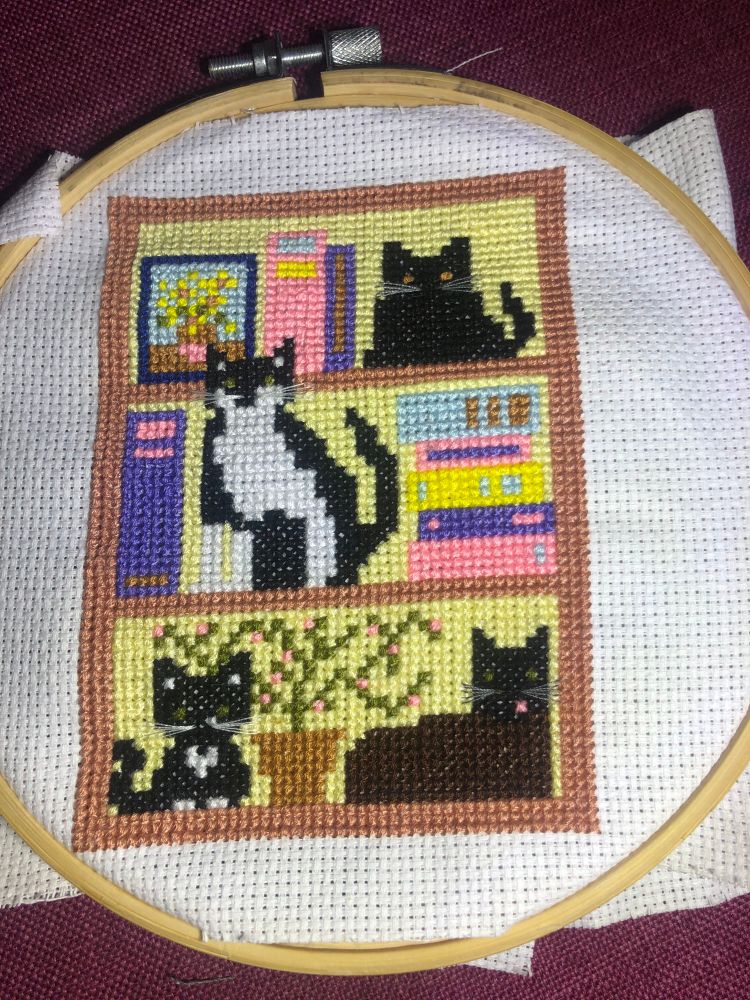 Completed cross stitch of four cats on a bookcase