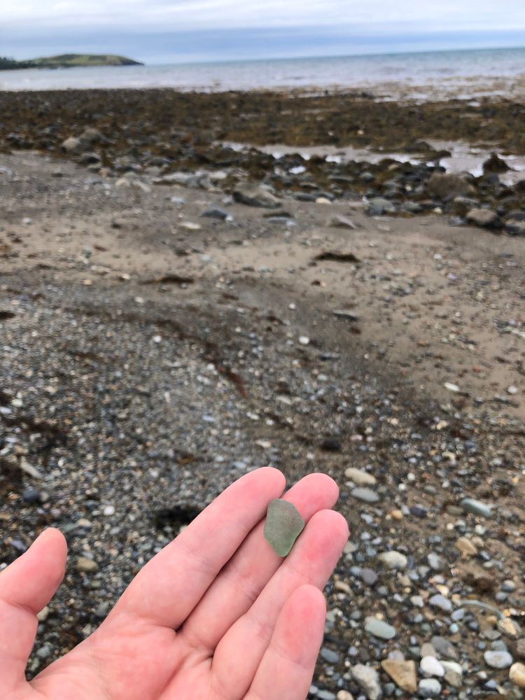 Hand holding piece of green sea glass on a rocky beach 