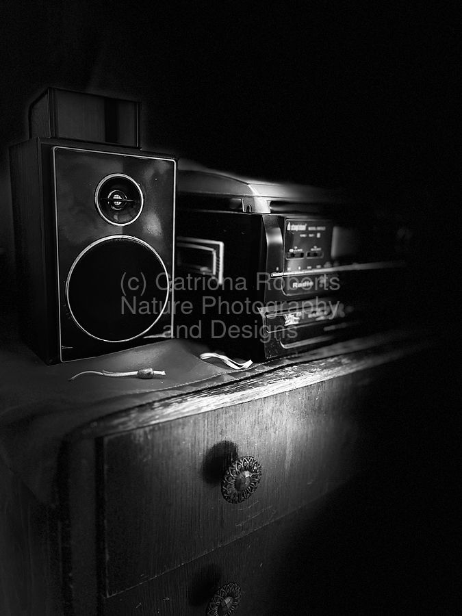 Digital  image featuring a black and white  photograph presenting the design Everyday Life's Moments- Distant Memories in Black and White. 
 A vintage radio, stereo and CD player rests on top of a wooden chest of drawers. 