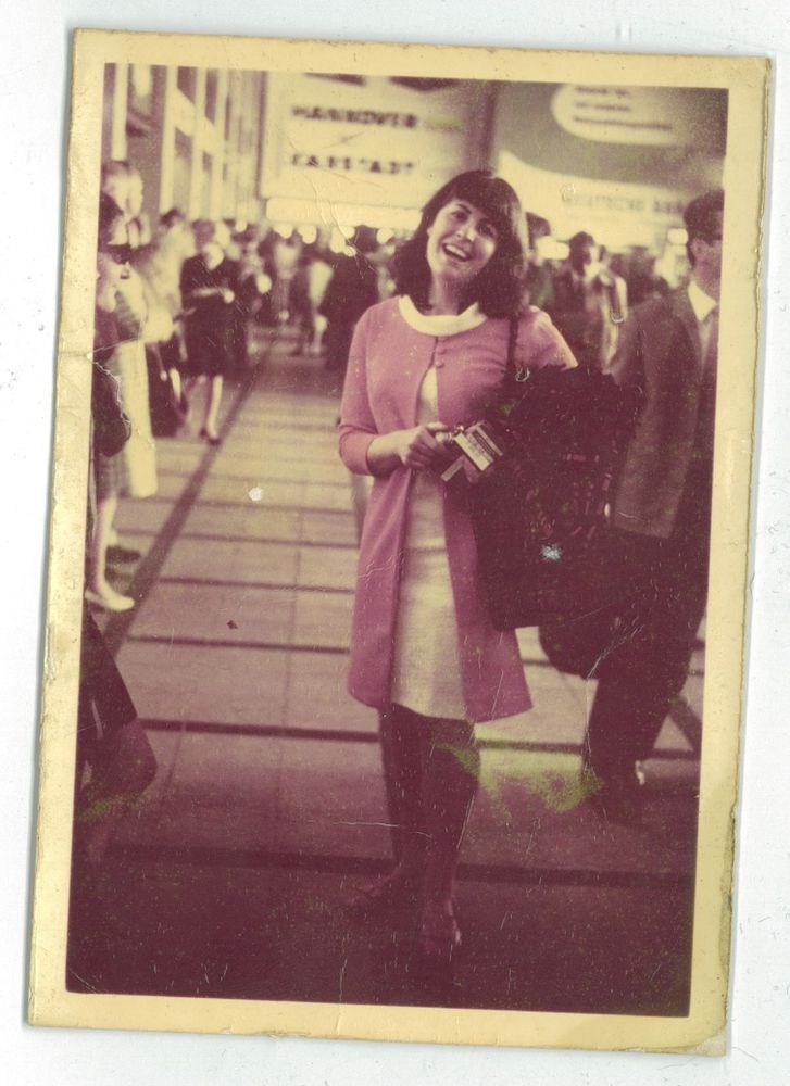 A picture of a dark haired woman in a pink coat smiling.