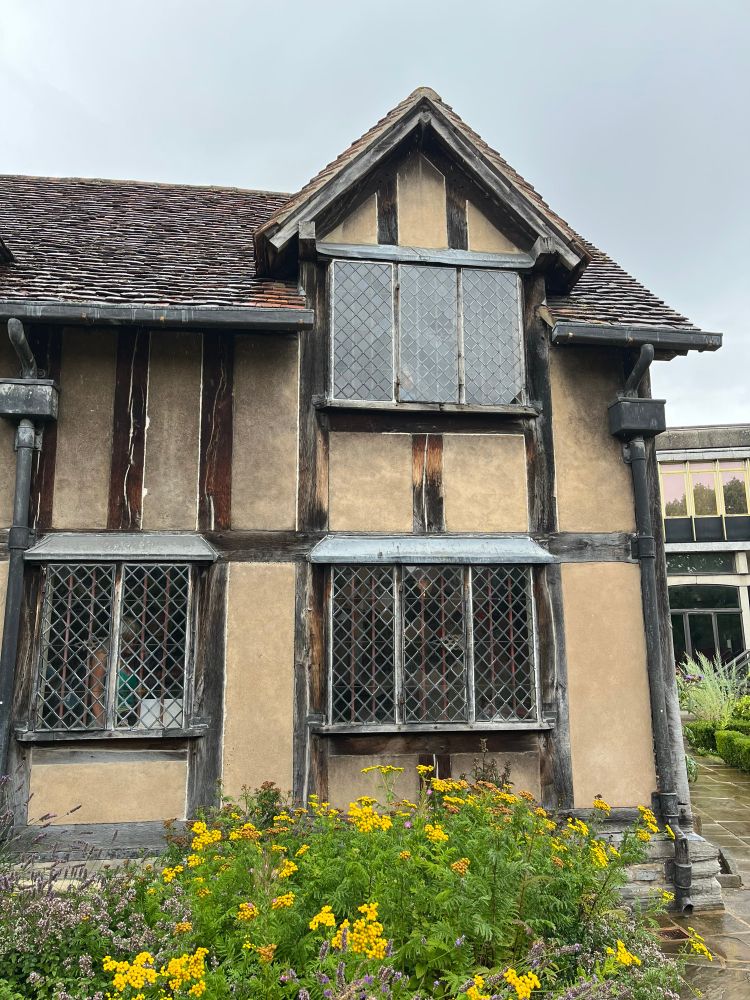 An old Tudor-styled house with glass windows and yellow flowers out front.