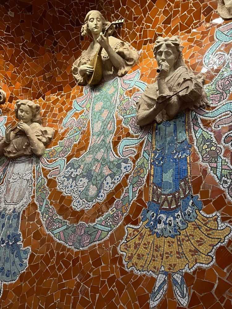 Three statues of women playing music are set against a tile mosaic.