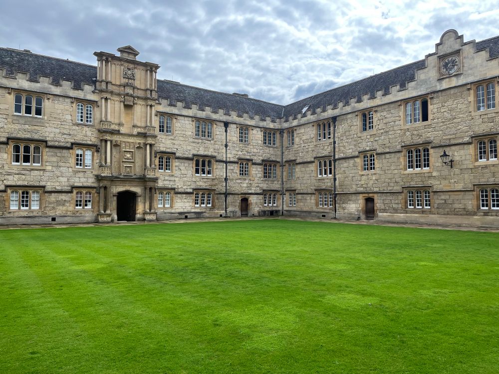 A college quad with a green lawn surrounded by sandstone buildings.