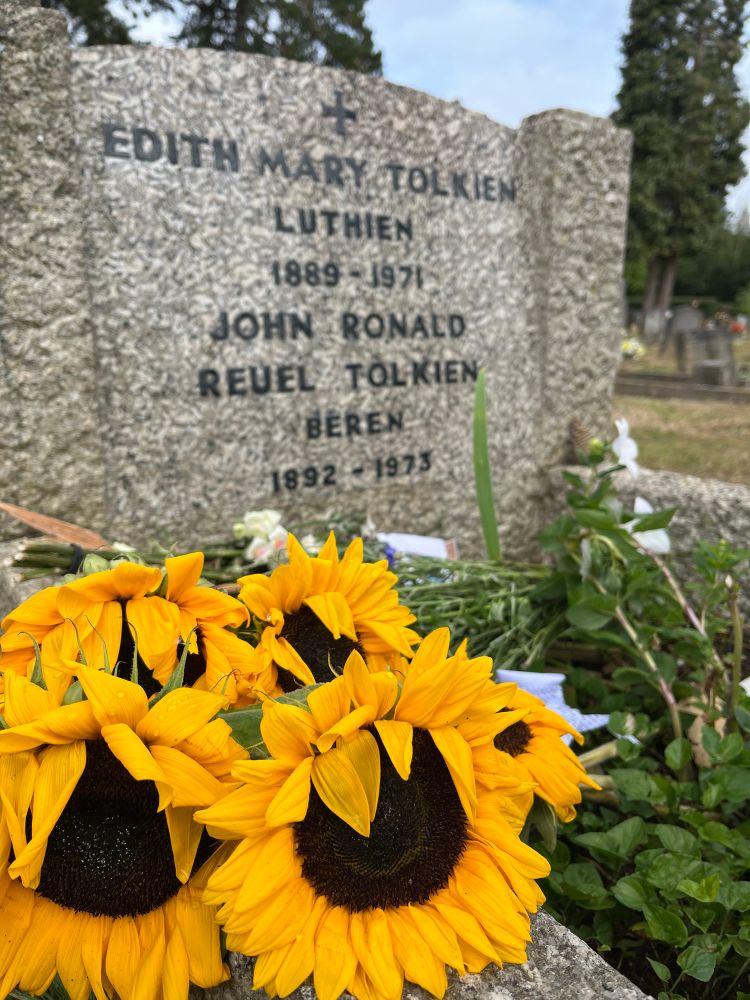 Sunflowers lie in front of a grave headstone that reads: Edith Mary Tolkien, Luthien, 1889-1971, John Ronald Reuel Tolkien, Beren, 1892-1973.