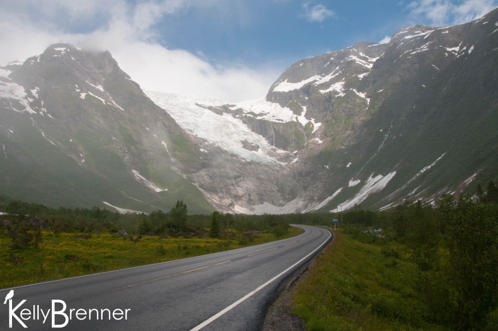 A road heading towards tall snow-covered mountains and a glacier
