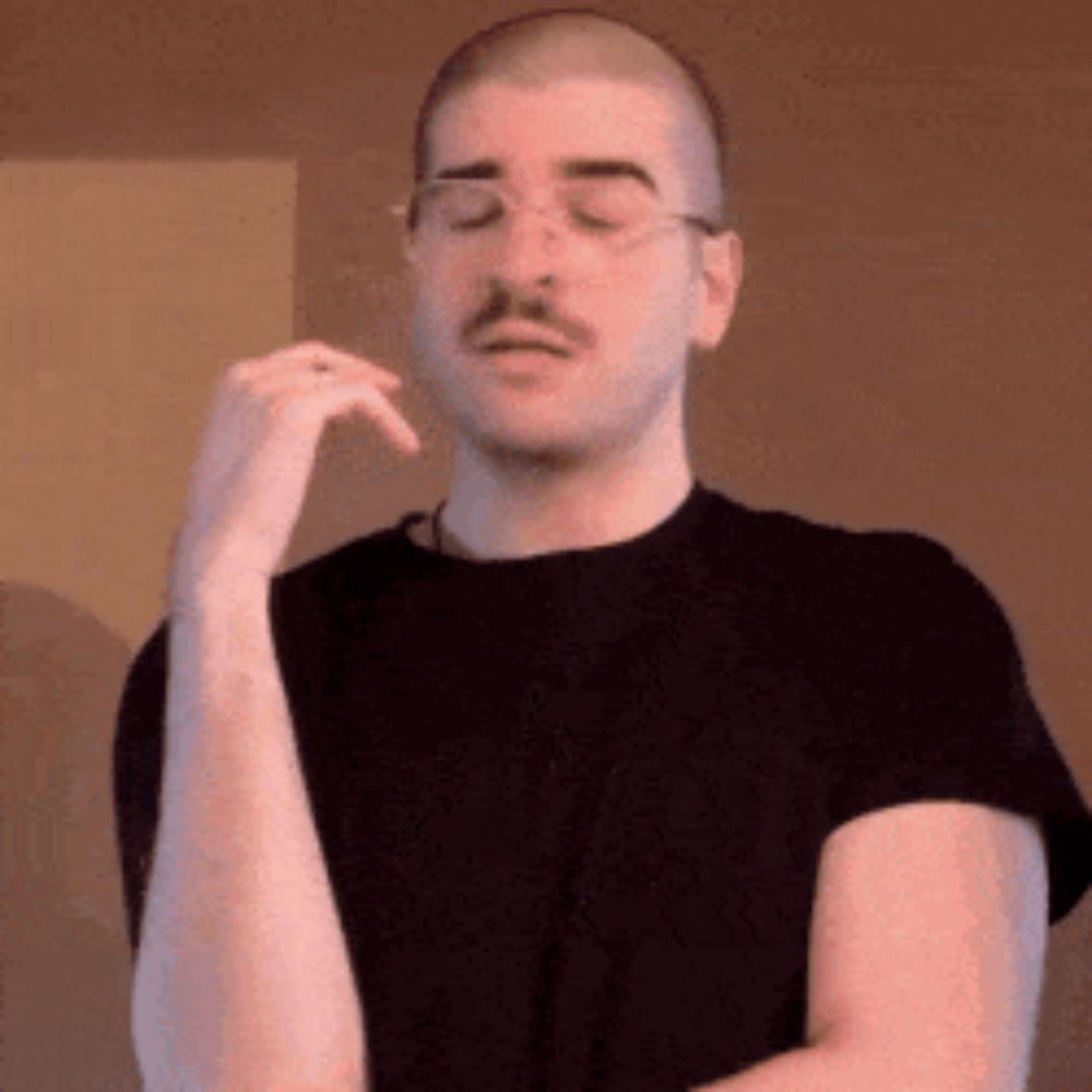 a man with a mustache and glasses is wearing a black shirt and making a funny face .