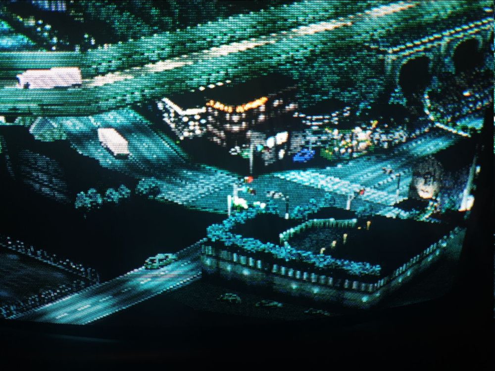 A crt tv screenie under RGB Scart of model railway-esque depiction of an isometric Yokohama with a road network, buildings, and trucks and other vehicles traveling around at night.