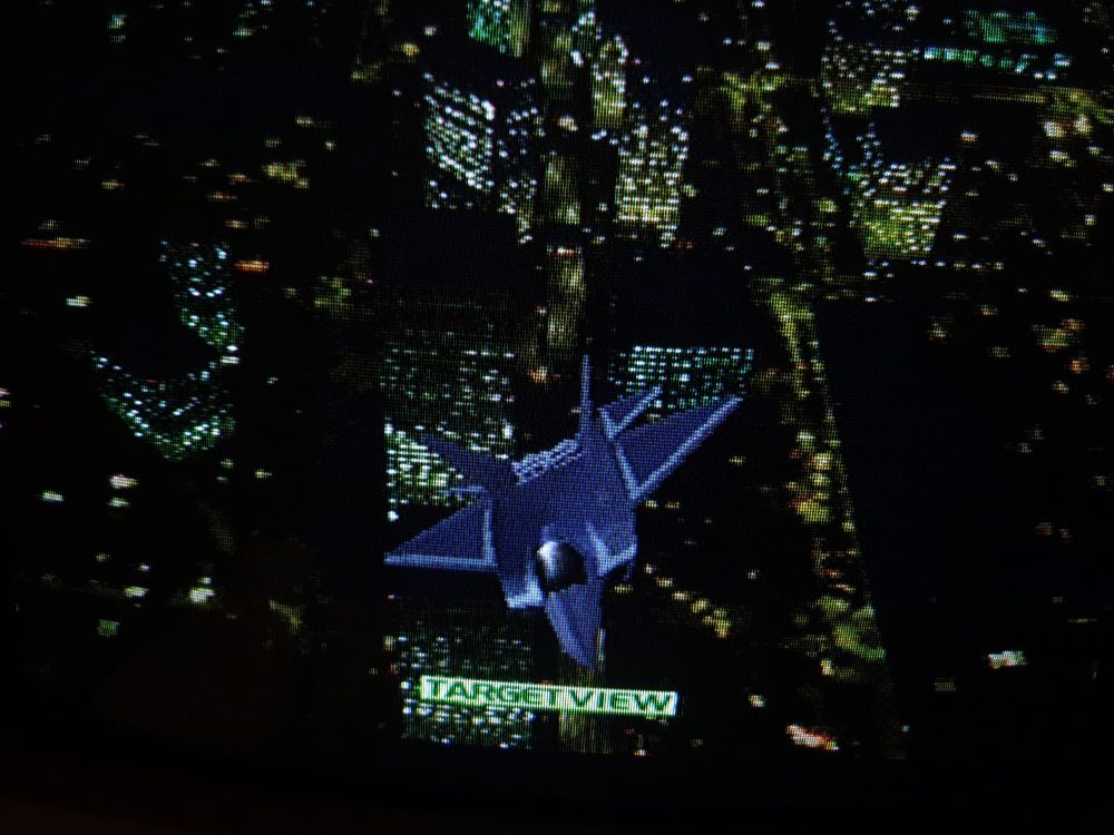 A CRT TV snap of one of the last levels in Ace Combat 2 with an F22 over a night time metropolis.