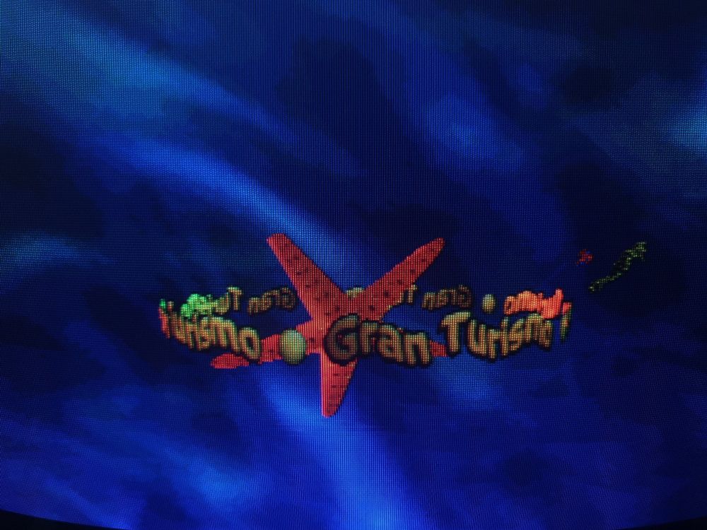 A crt screenie of a watery background ad polygon sealife, with Gran Turismo's demo represented by a starfish and gold wibblywobbly text