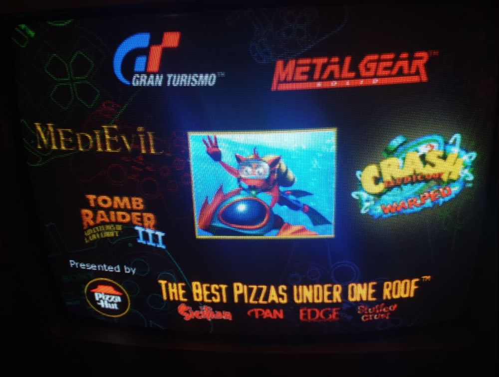A photo of the title screren with cool neon dual shock wireframe pads in the background and game logos around the central game preview window. Plus some Pizza Hut blurb at the bottom and the names of their hottest pizzas.