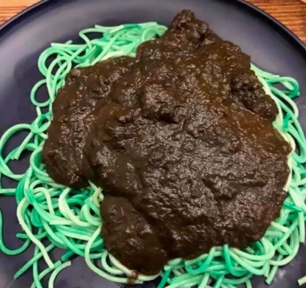 plate of green spaghetti with what looks like a dark brown mud pie splattered on top 