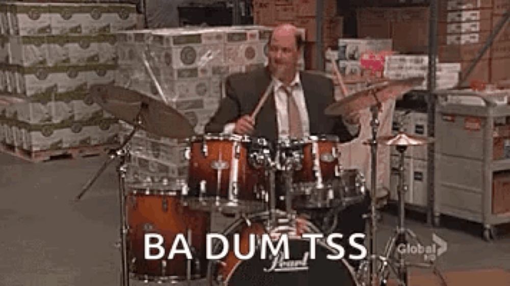 a man in a suit and tie is playing drums in a warehouse in front of boxes .