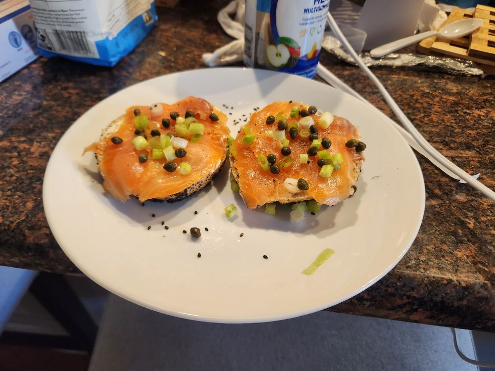 A sliced bagel with cream cheese, lox, scallions, and capers 
