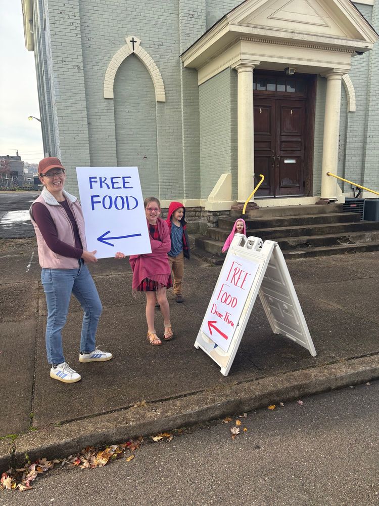 Free Food Drive Thru signs held by an adult white woman and her 3 small children. All smiles. 