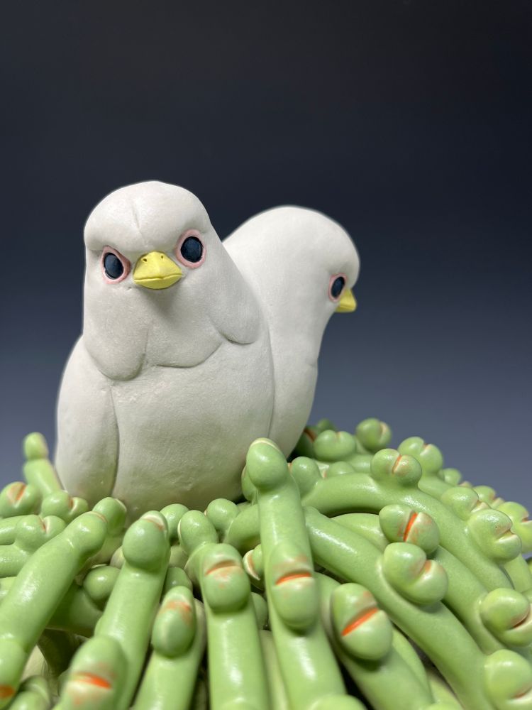 Ceramic sculpture detail of a two headed white bird with a yellow beak and black eyes on a green vining plant with orange details 