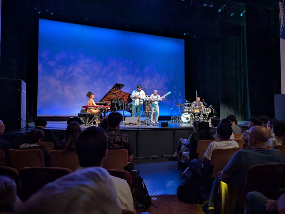 4-piece band playing on stage at UW. Left to right: piano, trumpet, electric bass, drums. Not pictured: audio moire patterns.
