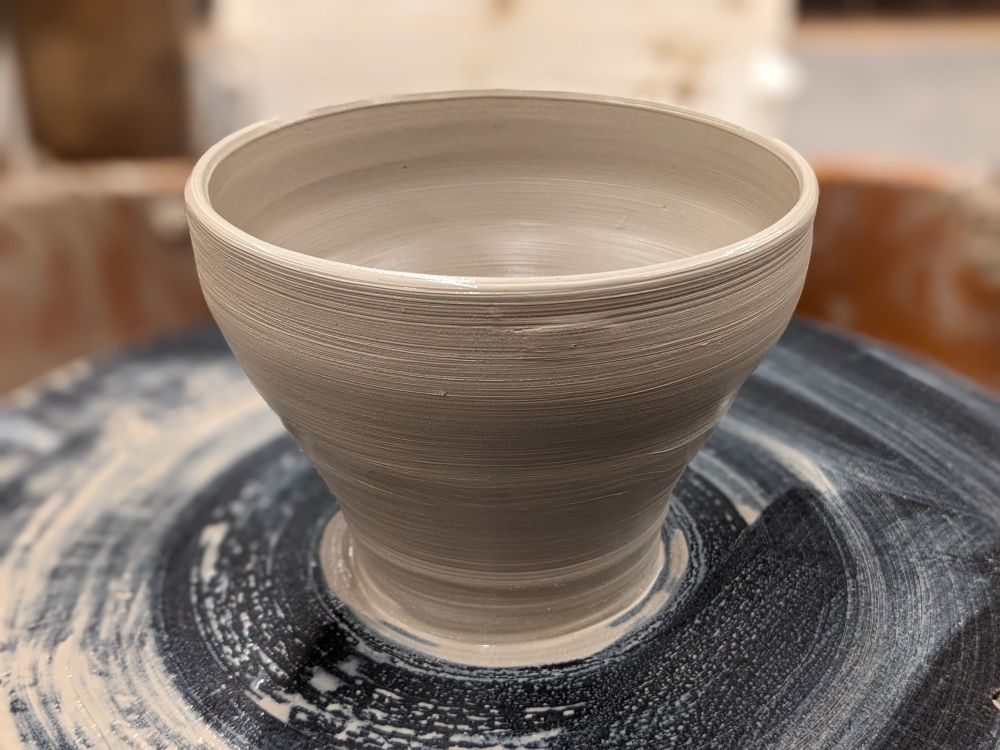Gray clay pot on a dirty pottery wheel.
