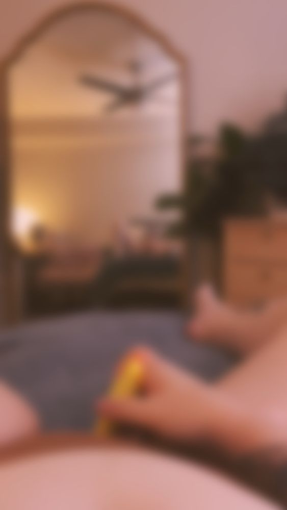 A blurred photo of gloss’ legs spread & using her yellow vibrator over her nude colored panties with the camera also pointed towards the full length mirror in front of her bed