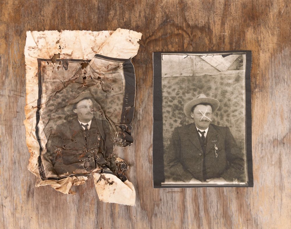 Two sepia prints on canvas against a worn brown wooden background. One is crumpled, stained red and eaten by termites and mould