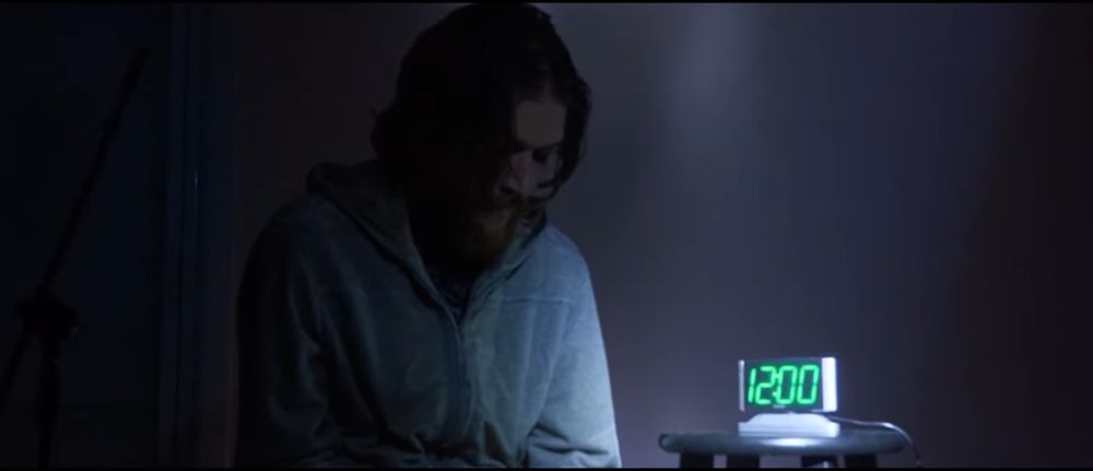 Bo Burnham, seen looking at a clock that reads 12:00. 