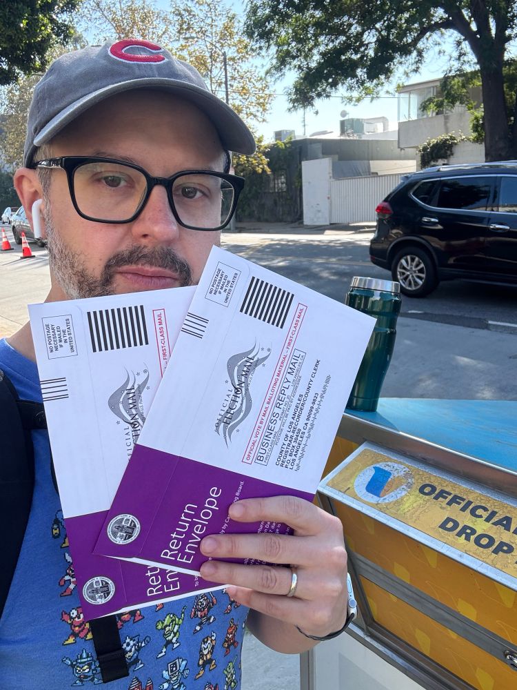 Me holding two mail ballots by deposit box 