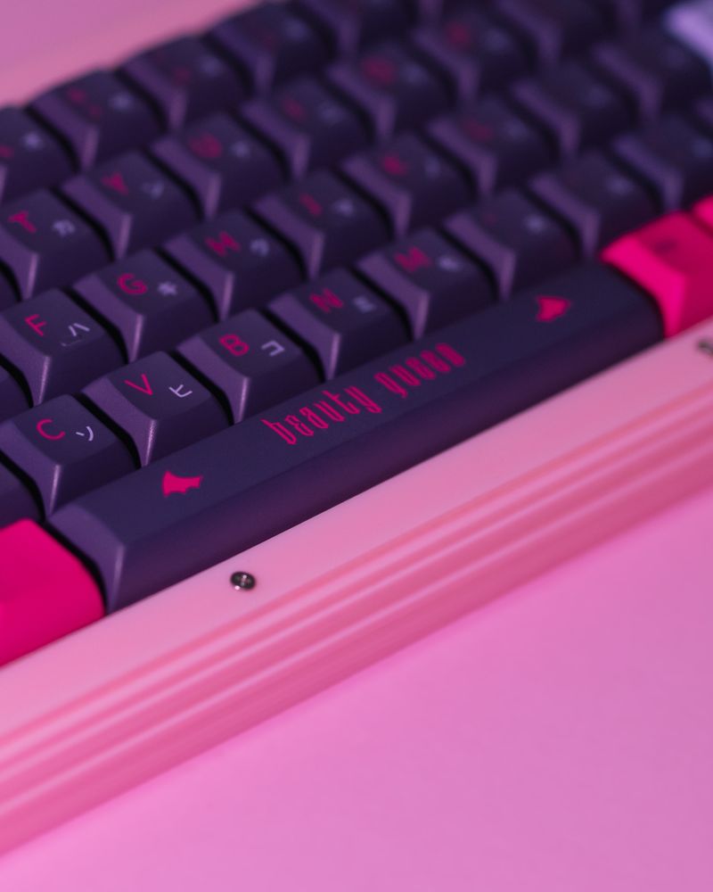 close-up of a pink keyboard with dark purple keycaps, hot pink and lavender blue legends and accents. the spacebar features the text 'beauty queen'