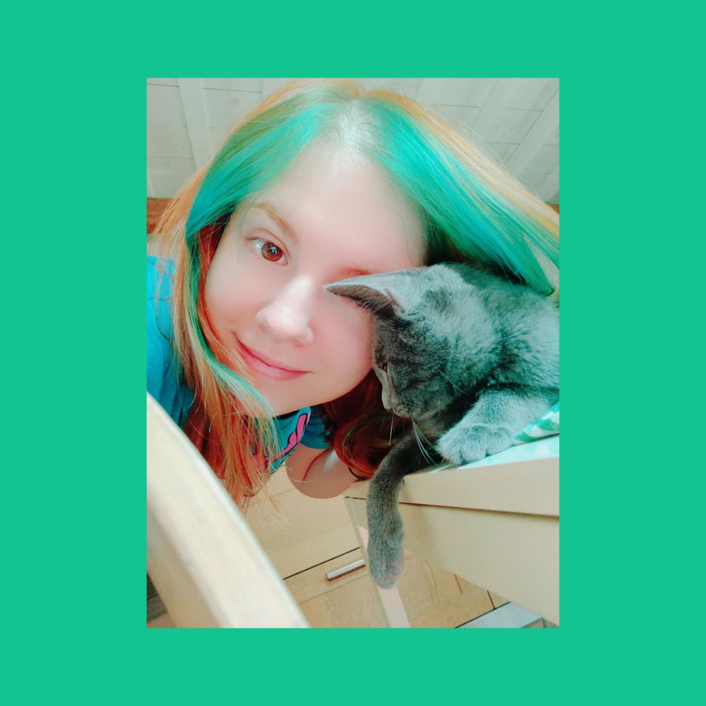picture of mari (blue t-shirt, orange and green hair) next to a tiny grey cat. color reflection kinda makes the cat look greenish as well