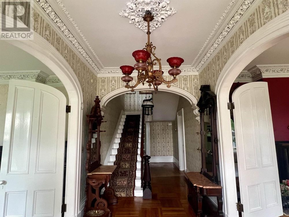 Entryway of an obviously-haunted house with red-tinted chandelier, creepy wallpaper and vintage furniture 